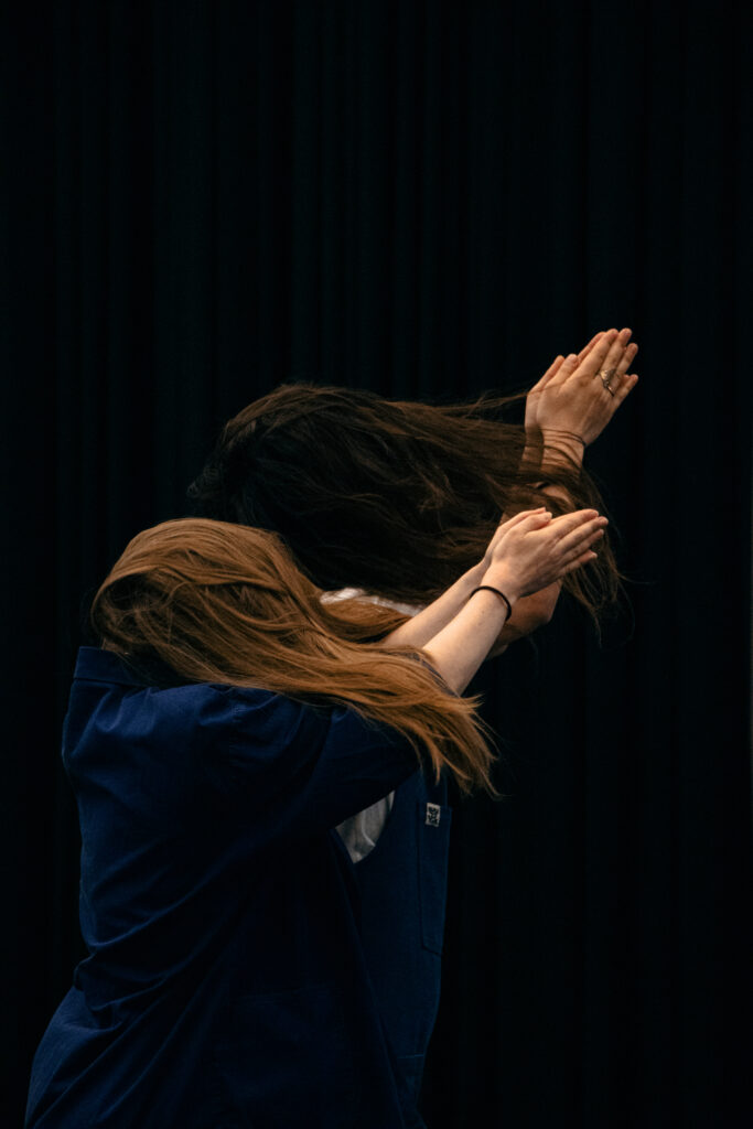 2 moving females with long hair hiding their face pointing towards the right corner with their arms 